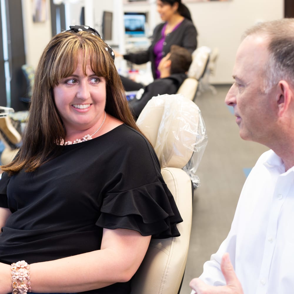 A woman sits in an exam chair and speaks with her Nalchajian Orthodontics team member.