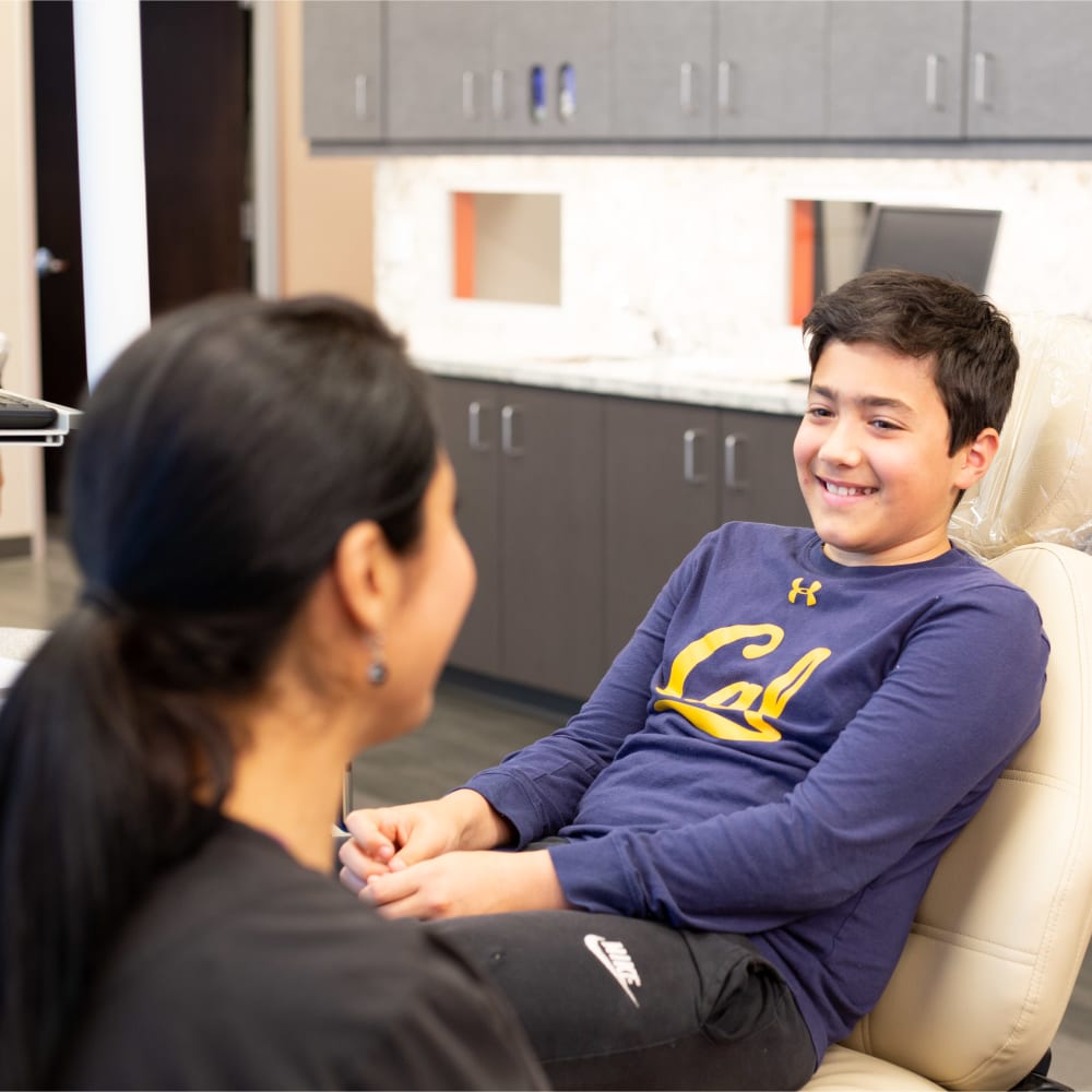A young patient sits in an exam chair and smiles at the Nalchajian Orthodontics team member sat across from him.