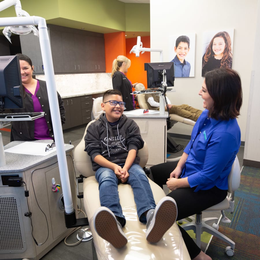 A young boy is sitting in a dental chair at Nalchajian Orthodontics and laughing with two team members.