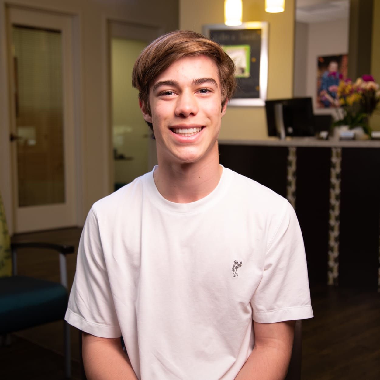 A teenage boy is sitting in the reception area at Nalchajian Orthodontics and smiling.