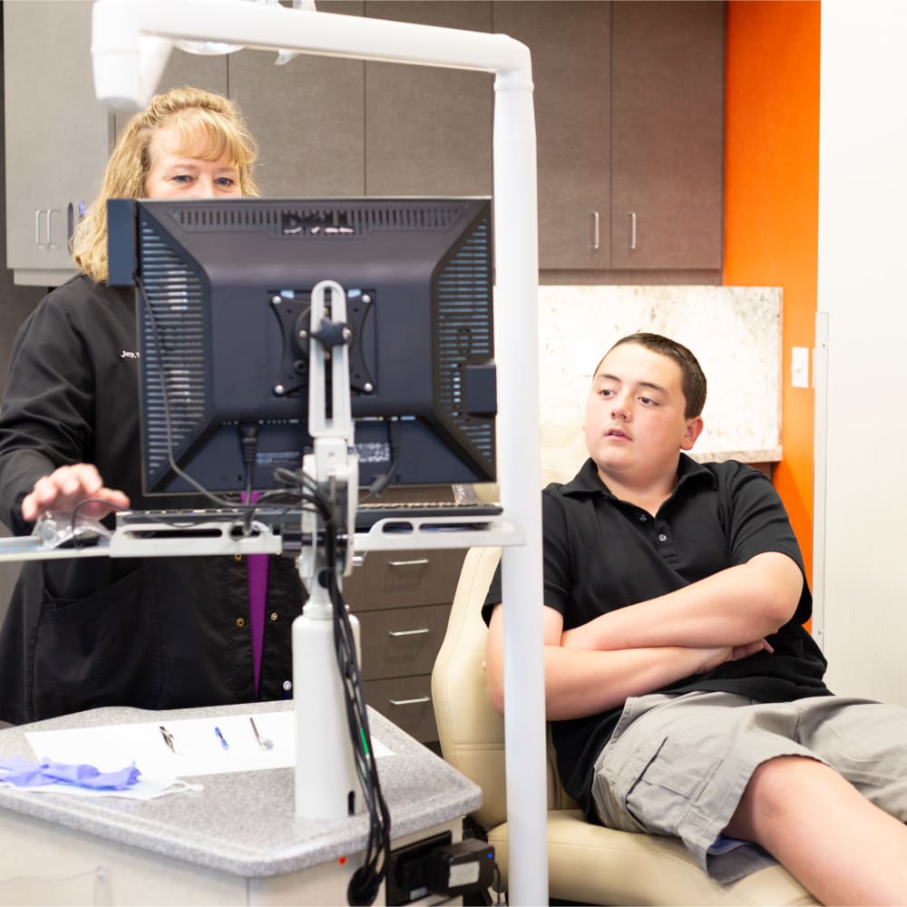 A teenage patient is in an exam chair, looking at the computer screen while his Nalchajian Orthodontics team member works away.